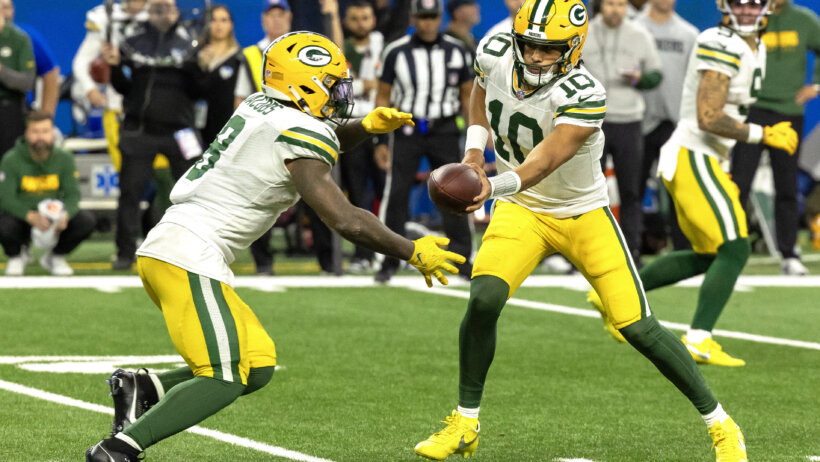 Green Bay Packers quarterback Jordan Love hands the ball off to running back Josh Jacobs