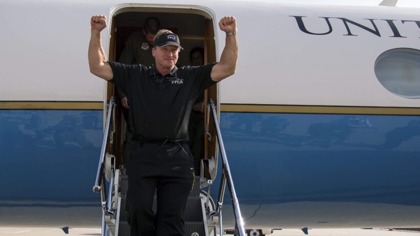 Jon Gruden getting off a plane with his arms in the air