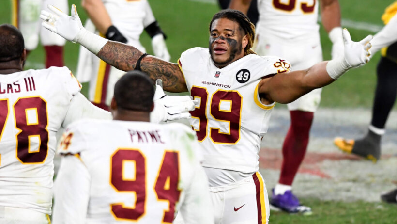 Washington Football Team defensive end Chase Young celebrating a win on the field with his arms wide open.