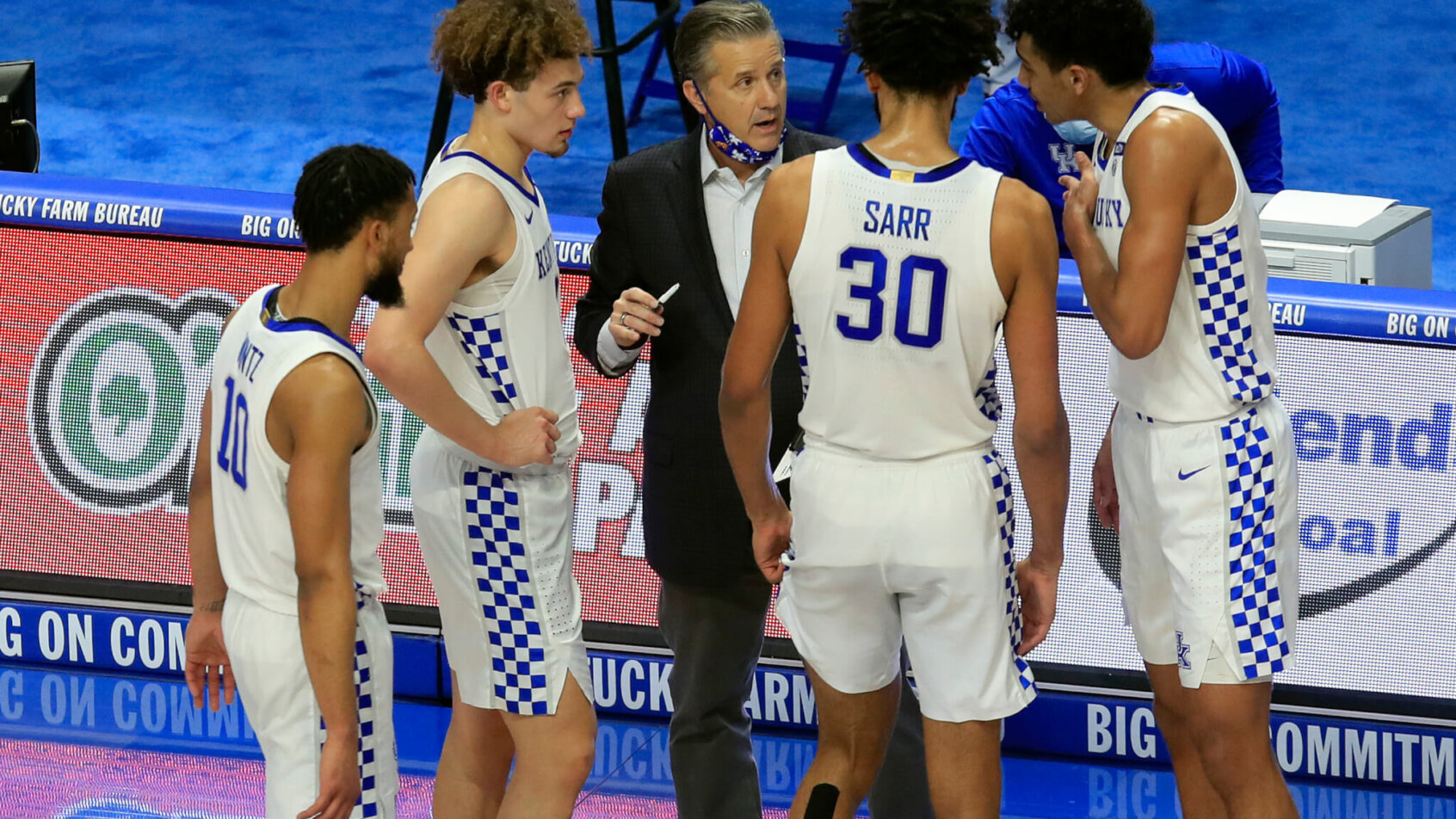 Kentucky's men's basketball head coach John Calipari talking to his players on the court during a stoppage of play during a game.