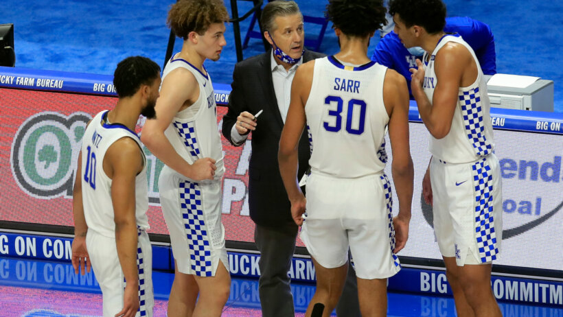 Kentucky's men's basketball head coach John Calipari talking to his players on the court during a stoppage of play during a game.
