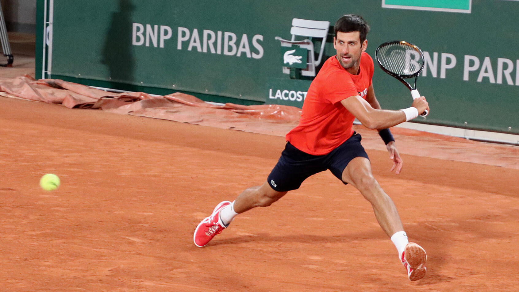 Novak Djokovic sliding to hit a backhand on clay