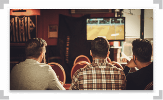 Three guys sitting at a bar watching TV