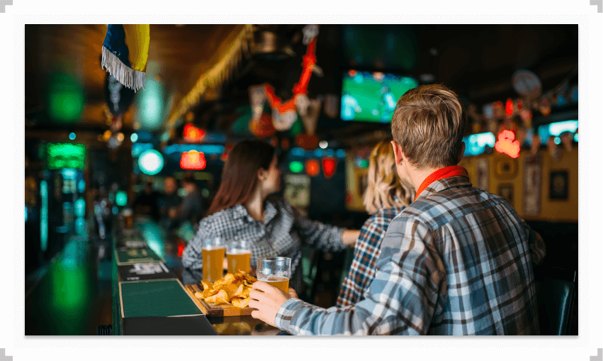 People sitting at a bar with drinks watching tv