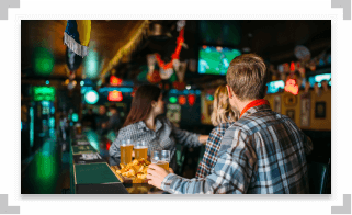 People sitting at a bar with drinks watching tv