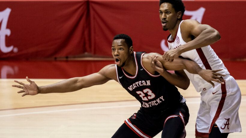 Western Kentucky center Charles Bassey and Alabama guard battling under the net during a basketball game.