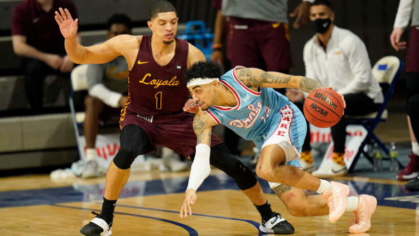 Drake guard Roman Penn driving past Loyola of Chicago's guard Lucas Williamson during a NCAA men's basketball game.