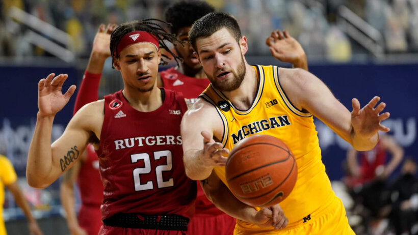 Rutgers guard Caleb McConnell and Michigan Wolverines center Hunter Dickinson battling for a loose ball during a NCAA men's basketball game.