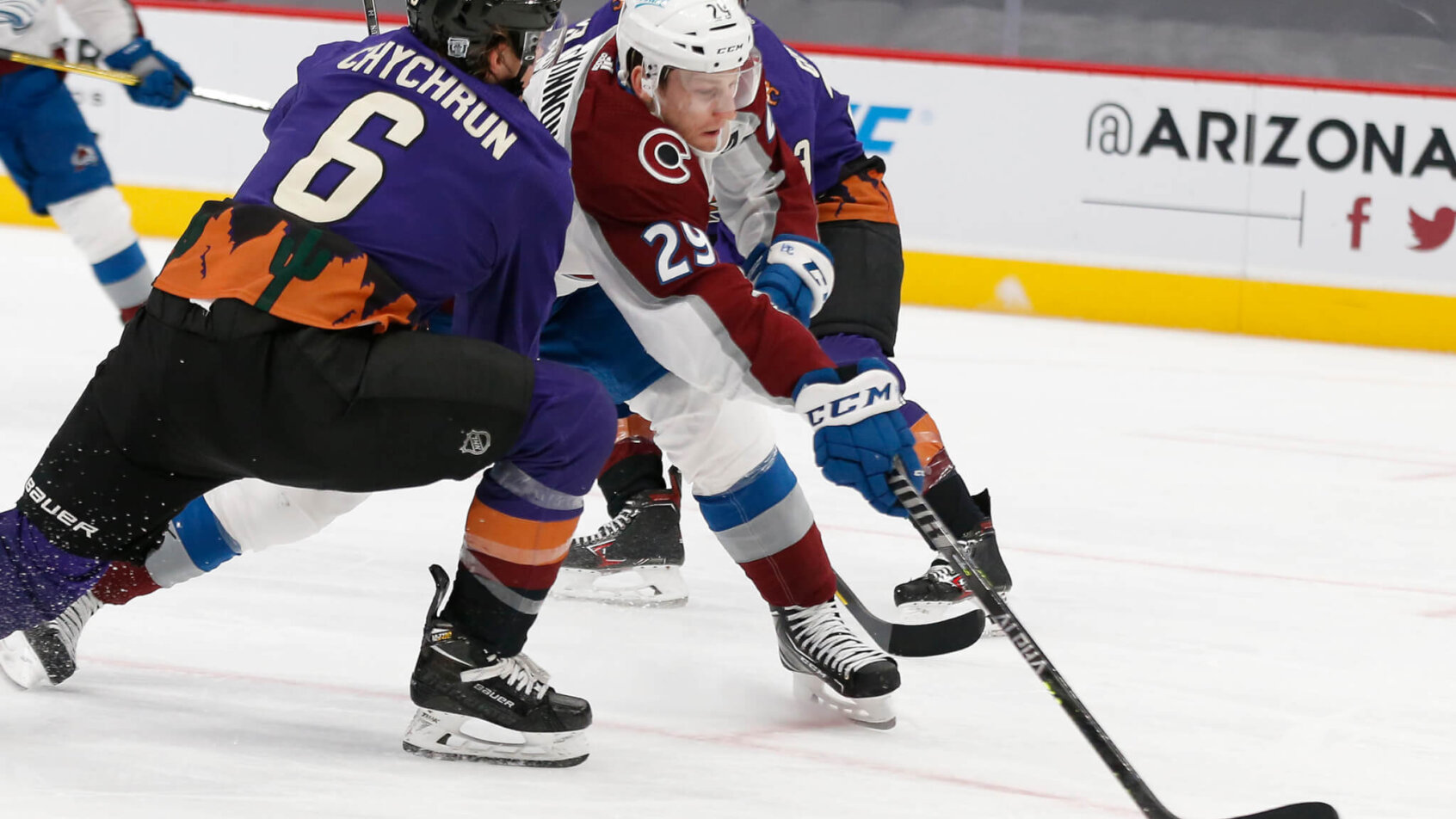Nathan MacKinnon trying to get a shot off between two Arizona Coyote players during a NHL game.