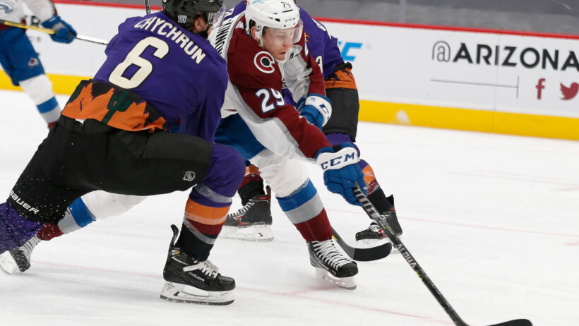 Nathan MacKinnon trying to get a shot off between two Arizona Coyote players during a NHL game.