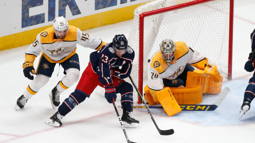 Nashville Predators' Alexandre Carrier trying to stop Columbus Blue Jackets' Cam Atkinson from taking a shot during an NHL game.