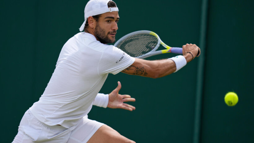 Matteo Berrettini hitting a backhand return during a Wimbledon tennis match.