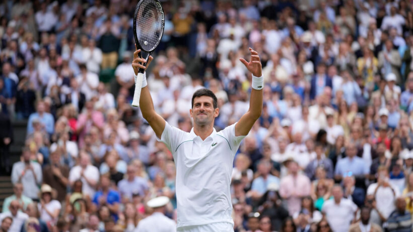 Novak Djokovic celebrating with his hands in the air after winning a match at Wimbledon.