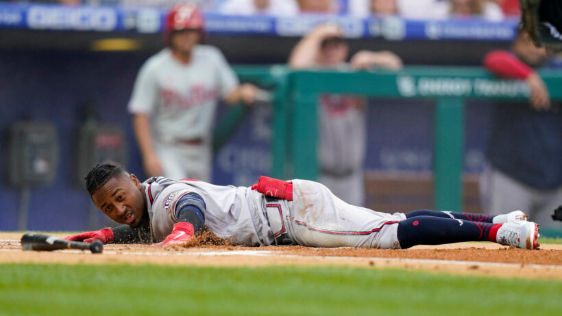 Atlanta Braves' Ozzie Albies stretched out on the ground over home plate after scoring a run during a baseball game.