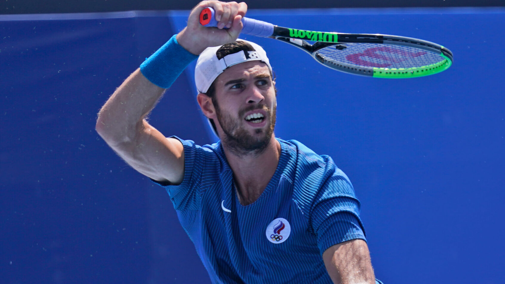 Karen Khachanov hitting a forehand return against an opponent during a tennis match at the Olympics.