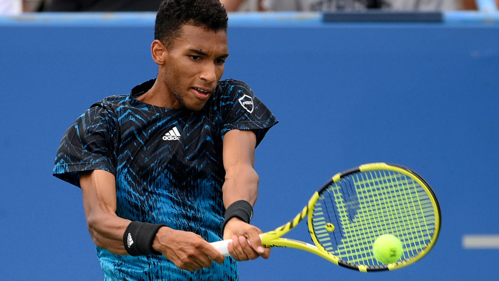 Felix Auger-Aliassime returning a shot during a tennis match.