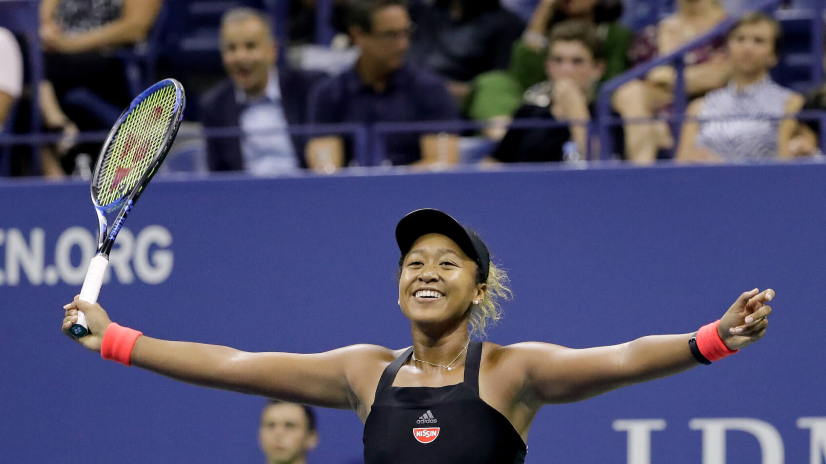 Naomi Osaka celebrating with her arms out after winning a tennis match.