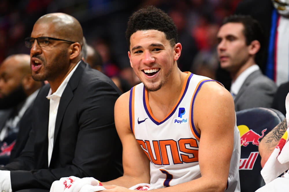 Phoenix Suns guard Devin Booker sitting on the bench smiling.