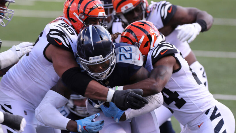 Tennessee Titans' Derrick Henry being tackled by Cincinnati Bengals' players.