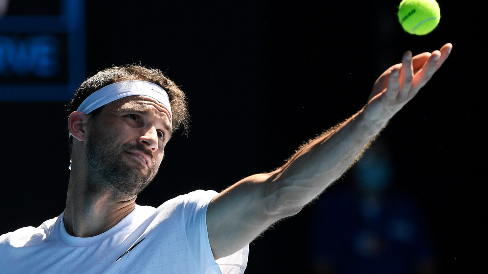 Grigor Dimitrov throwing the ball up in the air for a serve during a tennis match.
