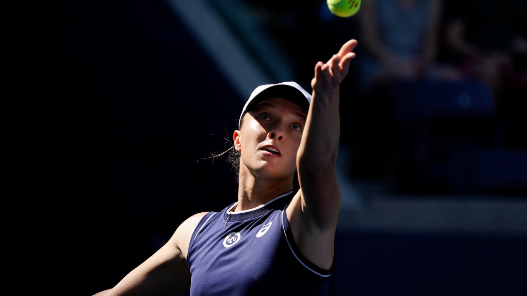 Iga Swiatek throwing the ball up to serve during a tennis match.
