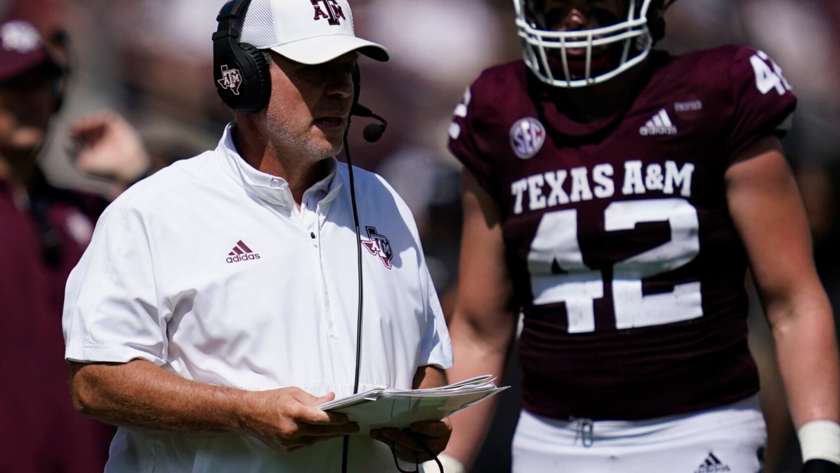 Texas A&M head coach calling a play with a player during a college football game.