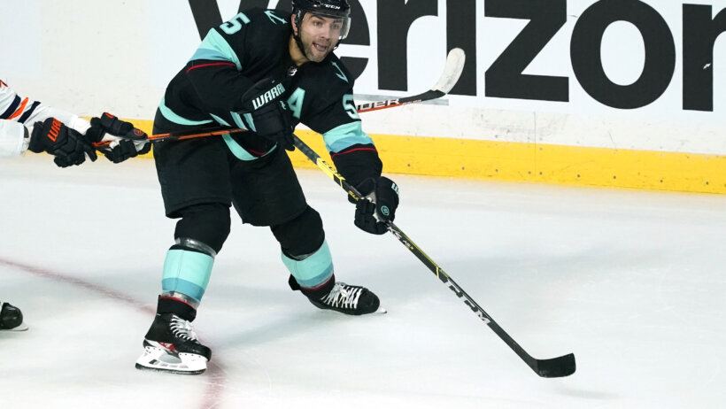 Seattle Kraken's Jeremy Lauzon reaching for the puck during a preseason NHL game.