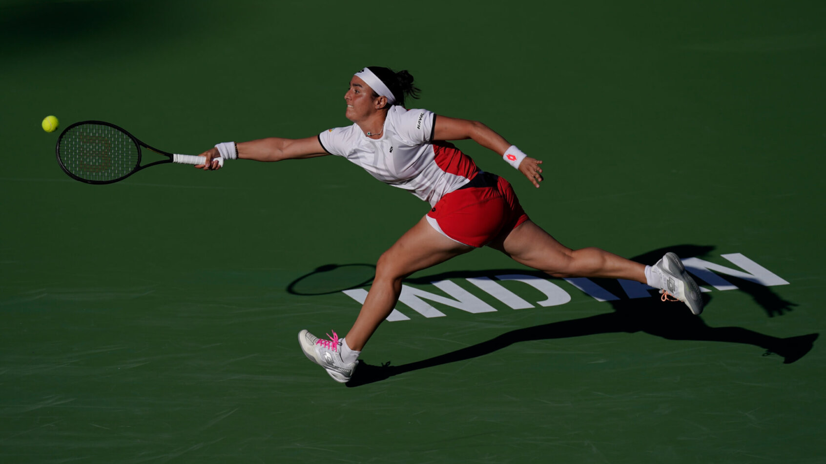 Ons Jabeur stretching to reach a ball to hit a return shot during a tennis match.