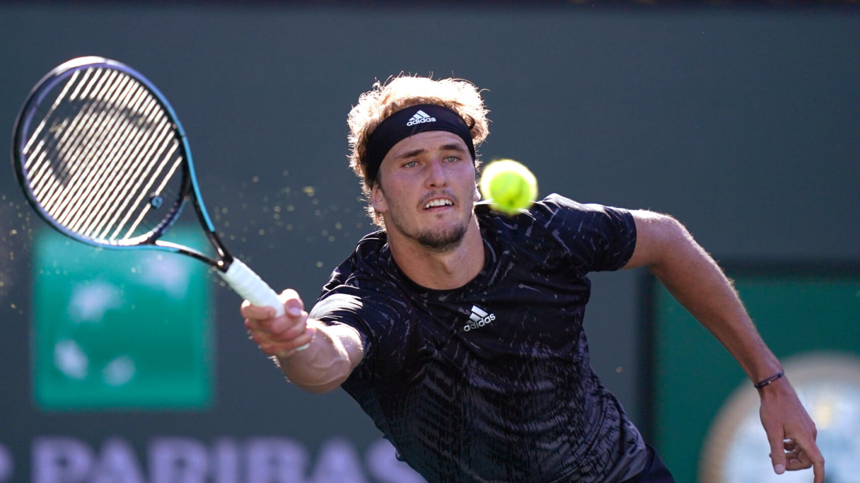 Alexander Zverev reaching to hit a return shot during a tennis match.