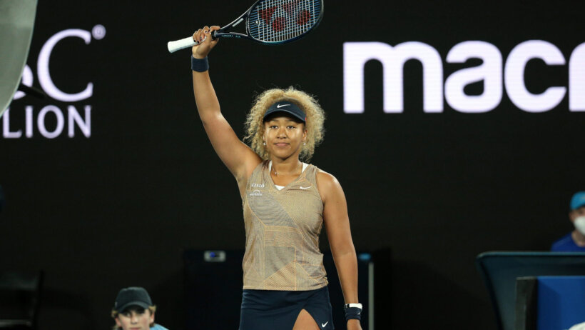 Naomi Osaka with her arm and racket in the air after winning a tennis match.