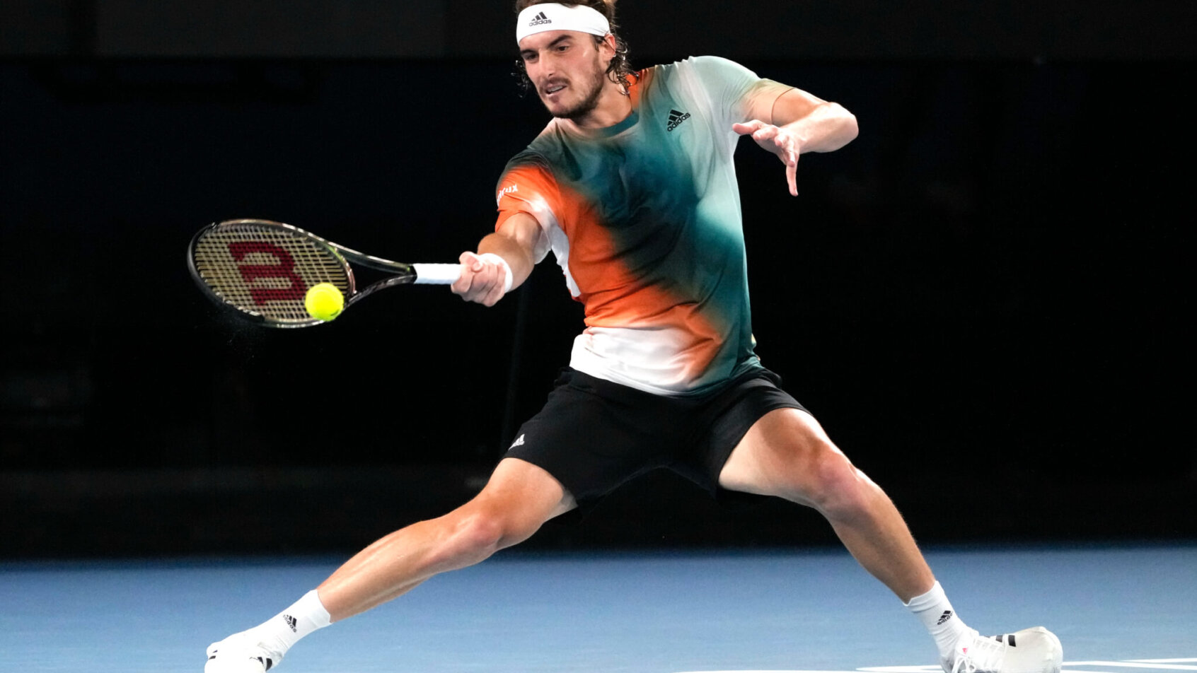 Stefanos Tsitsipas stretching to hit a forehand return during a tennis match.