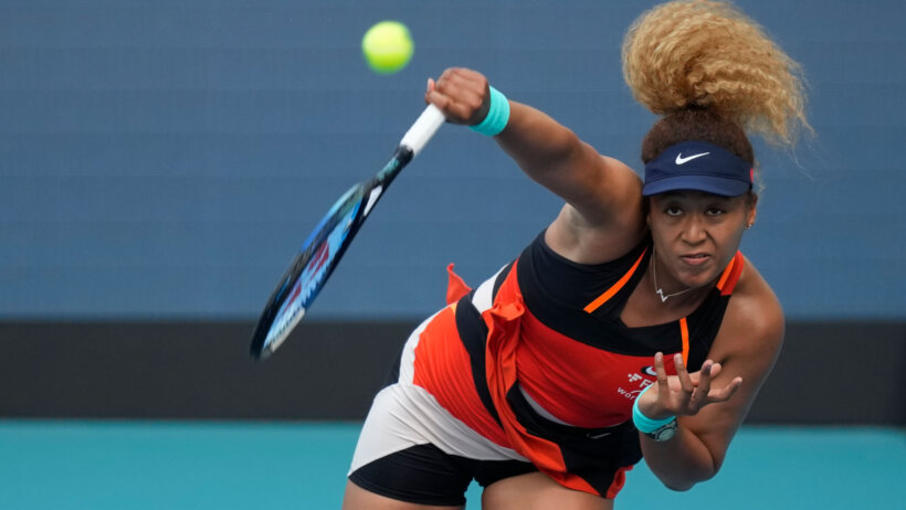 Naomi Osaka hitting a serve during a match at the 2022 Miami Open.