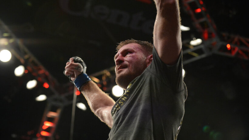 Stipe Miocic arms up celebrating sitting on UFC Octagon cage