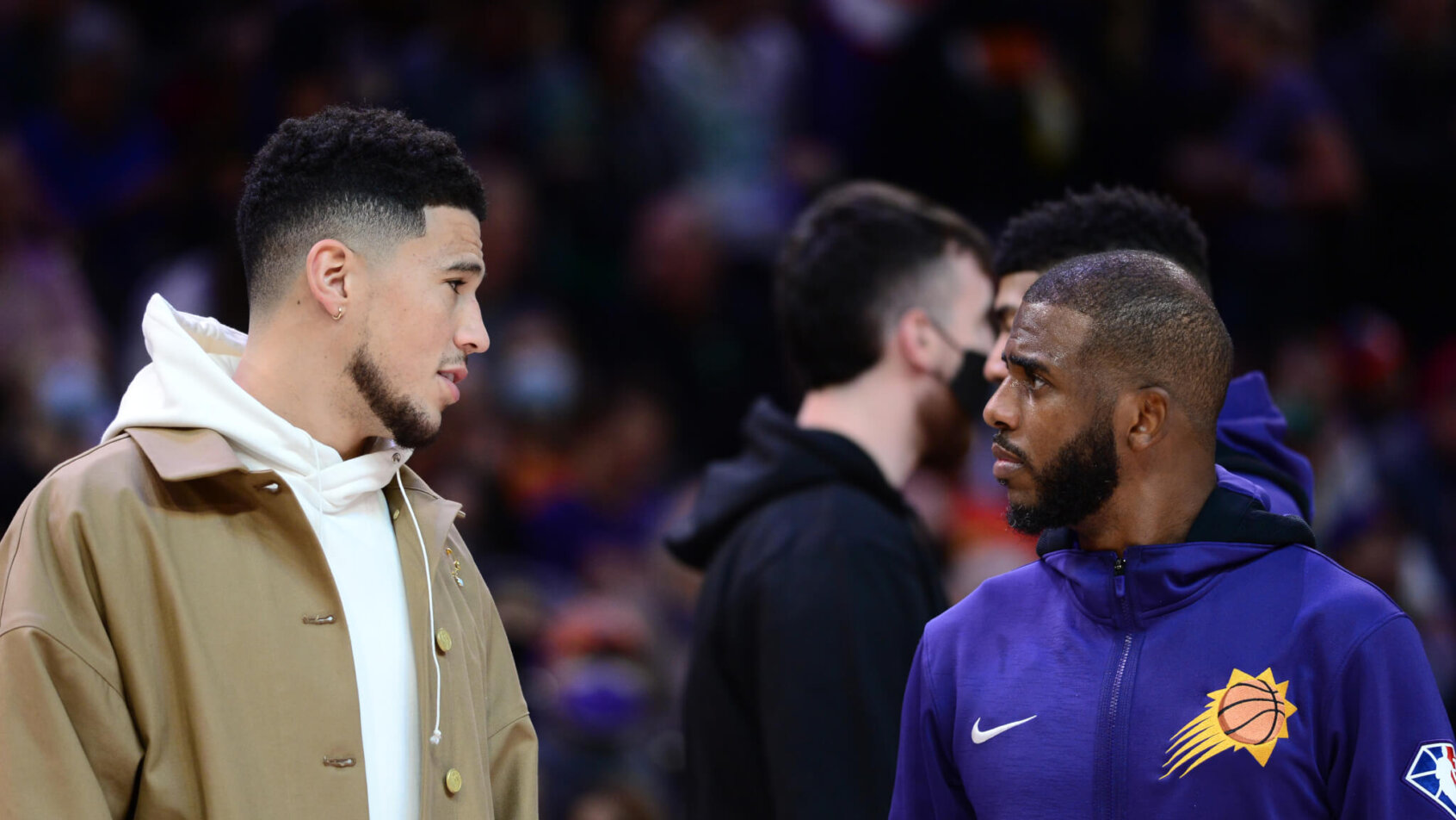 Devin Booker in street clothes talking to Chris Paul