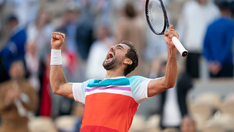 Marin Cilic celebrating with his hands in the air after winning a tennis match.