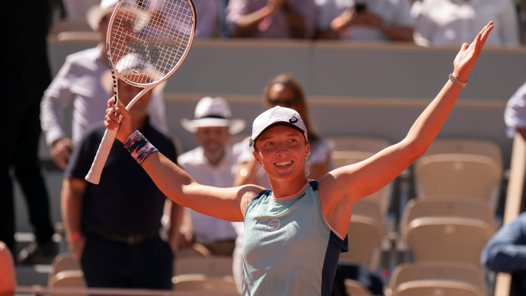 Iga Swiatek celebrating with her hands in the air after winning a match.