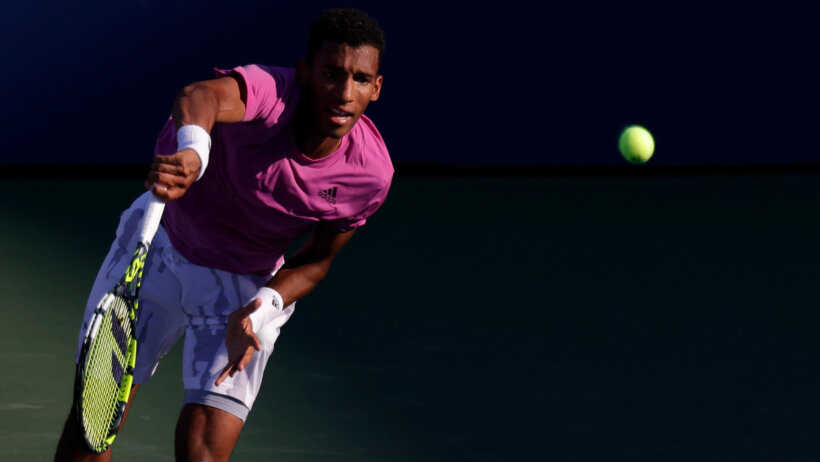 Felix Auger-Aliassime serving a ball during a tennis match.