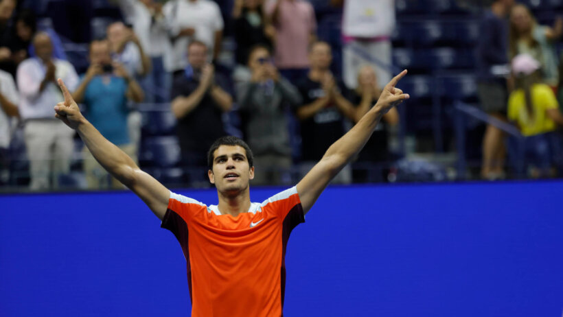 Carlos Alcaraz with his hands in the air looking at the crowd.