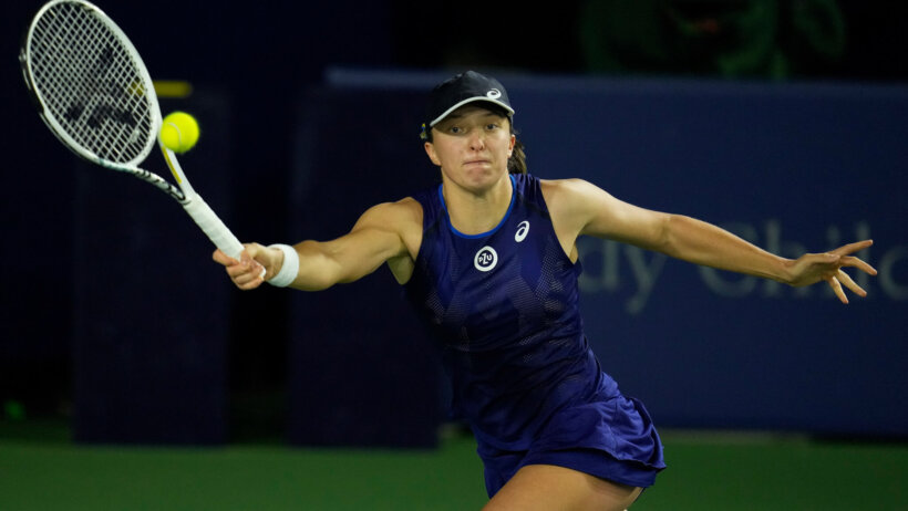 Iga Swiatek stretching to hit a forehand shot during a tennis match.