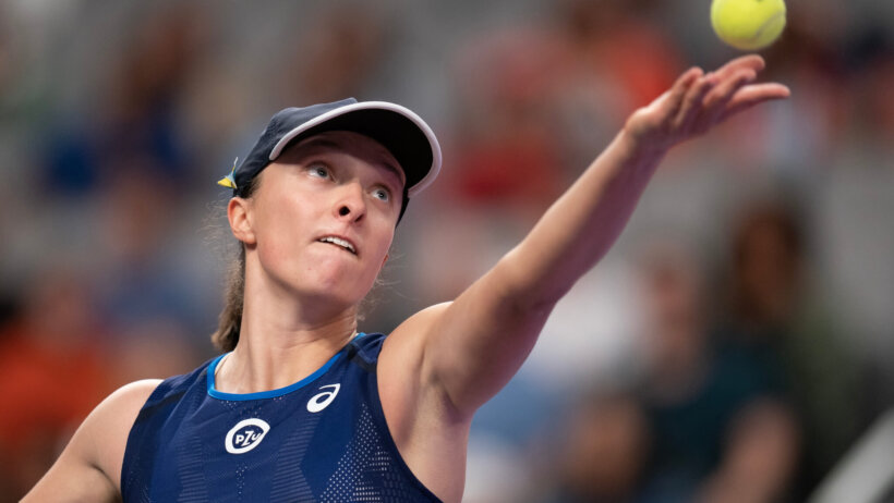 Iga Swiatek tossing the ball to serve the ball during a tennis match.