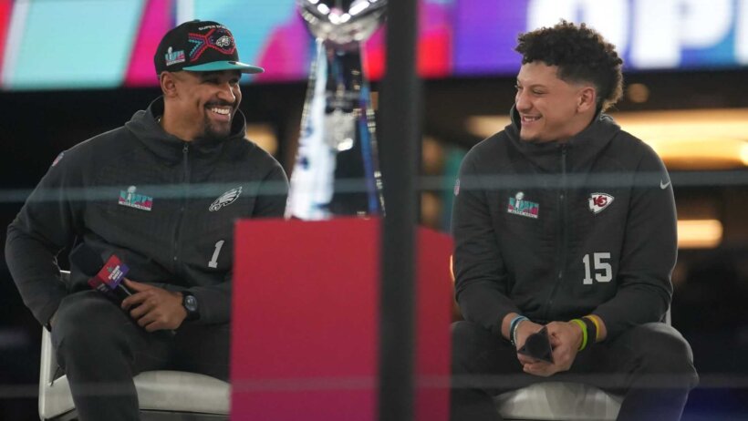 Jalen Hurts Patrick Mahomes sitting holding microphones beside Vince Lombardi Trophy