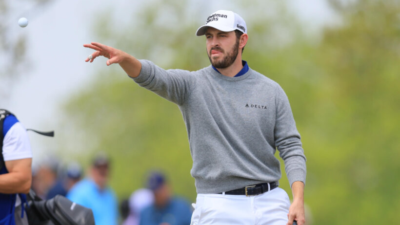 Patrick Cantlay throws a golf ball to his caddie