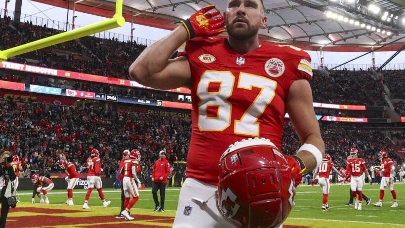 Travis Kelce hand behind ear holding helmet red jersey