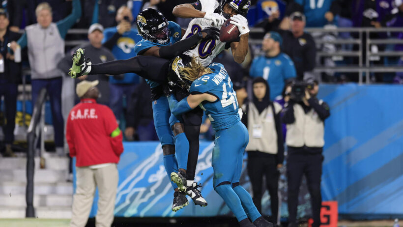 Ravens tight end Isaiah Likely hauling in a pass between two Jaguars defenders.