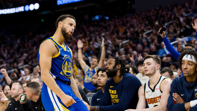Golden State Warriors guard Stephen Curry poses in front of the Denver Nuggets bench