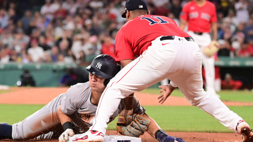 New York Yankees shortstop Anthony Volpe sliding into third as Boston Red Sox third baseman Rafael Devers tries to tag him out