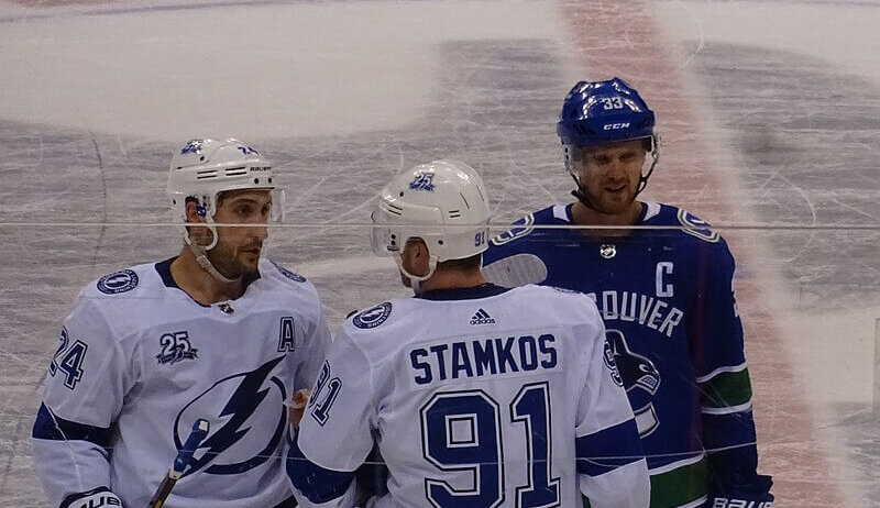 Steven Stamkos at center ice flanked by a teammate and Henrik Sedin